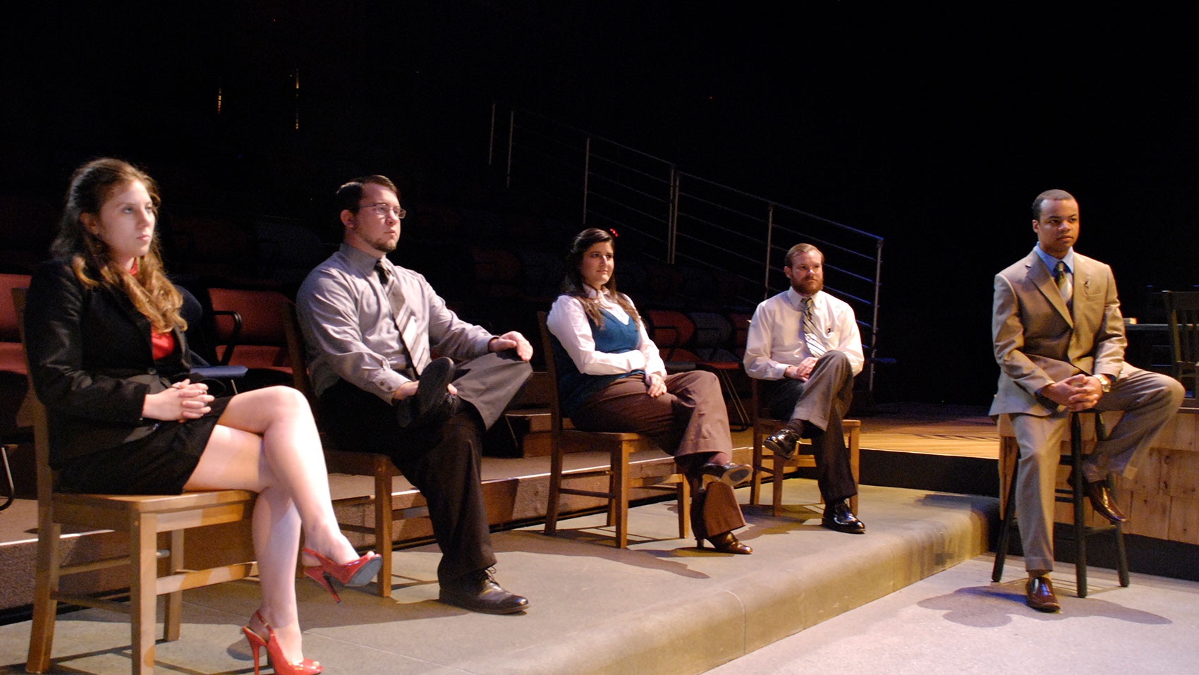 A group of five characters sit in a line, the first four on wooden chairs and the last character on a wooden stool. 