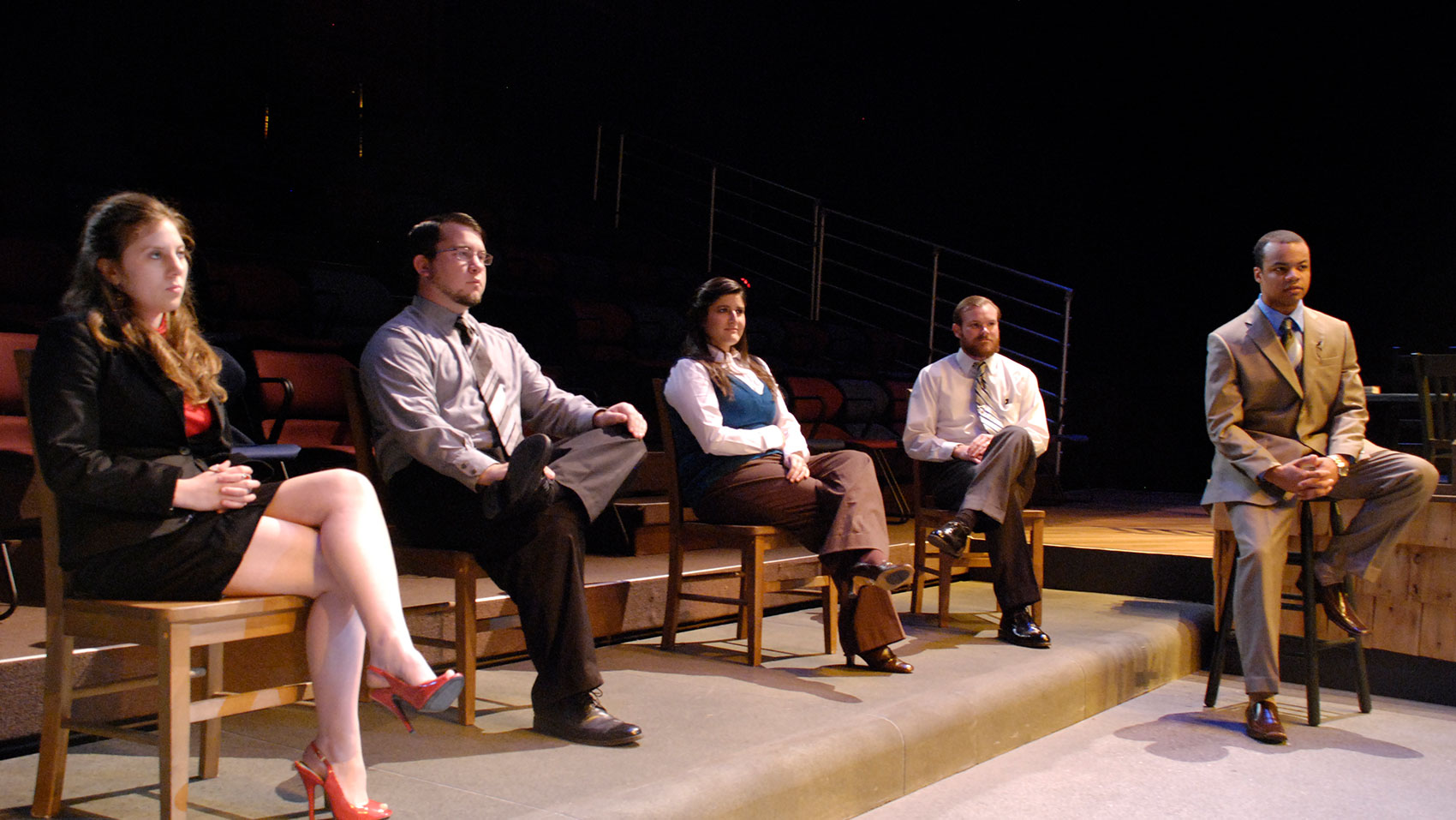 A group of five characters sit in a line, the first four on wooden chairs and the last character on a wooden stool.