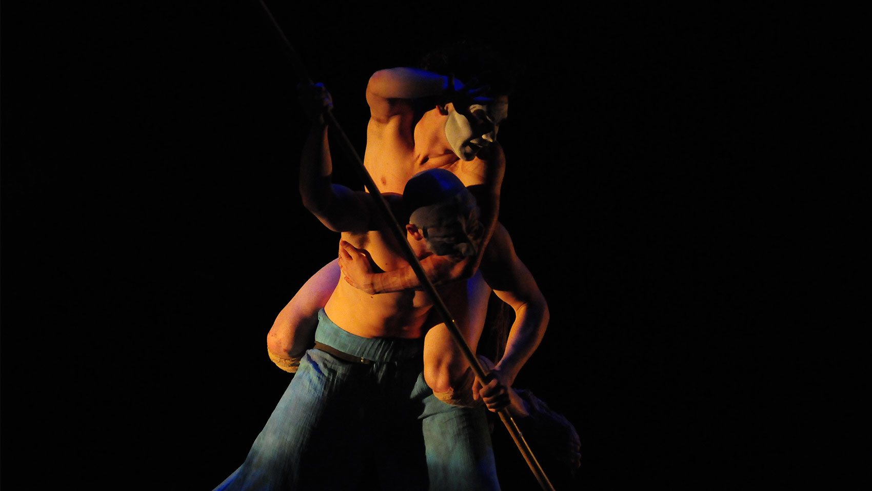 Two men in white face paint entangled with each other