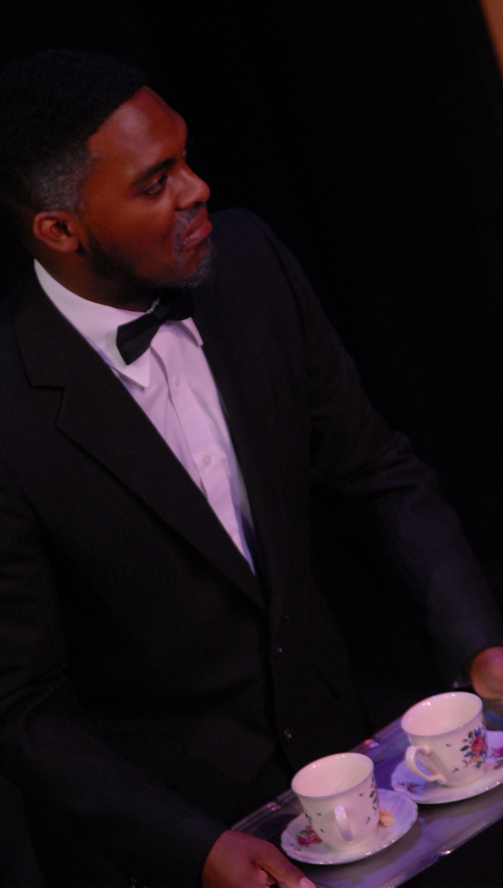 A character in a suit holds a tray of two teacups.