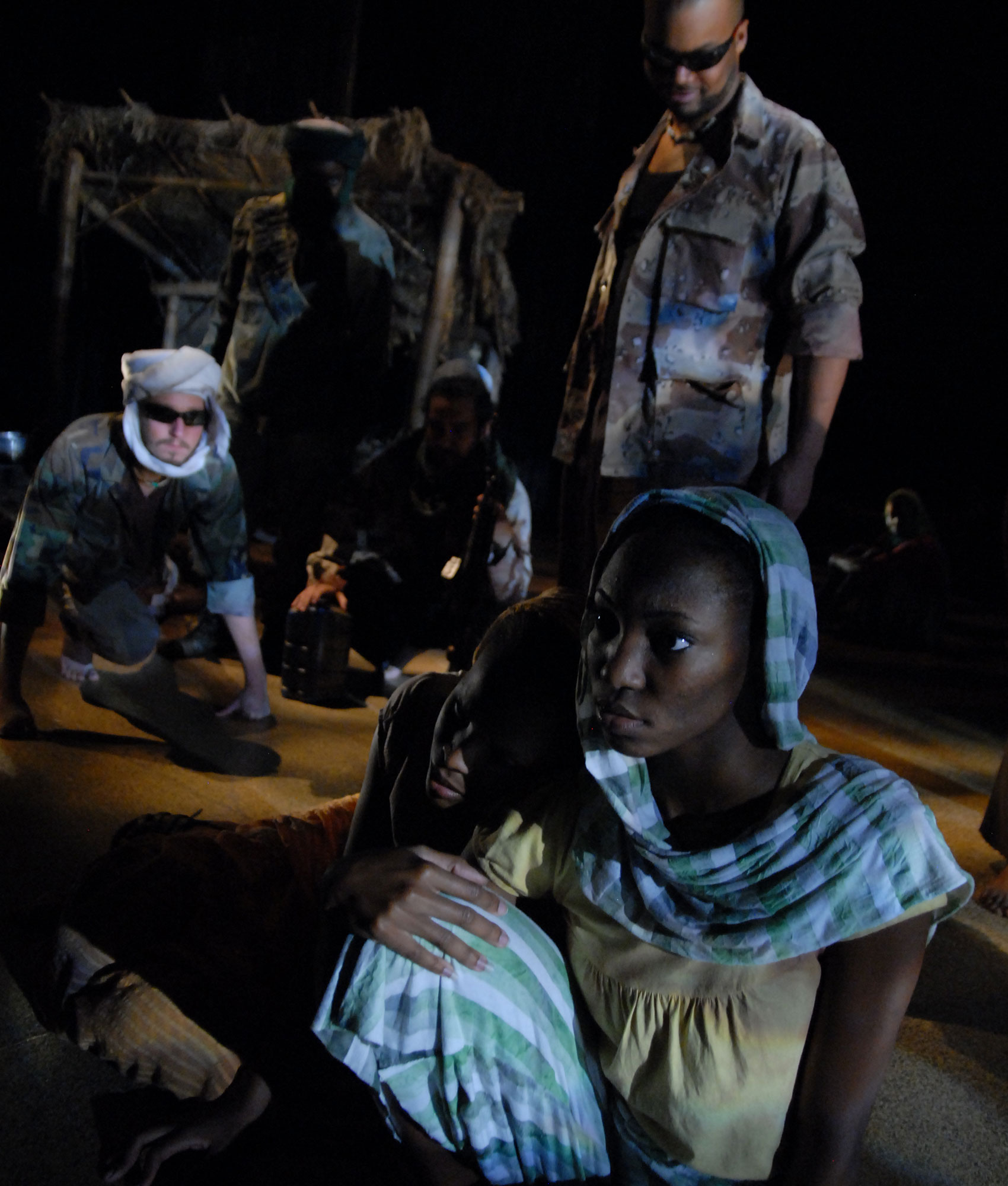 A woman leaning on another woman while a man in military gear stares at them