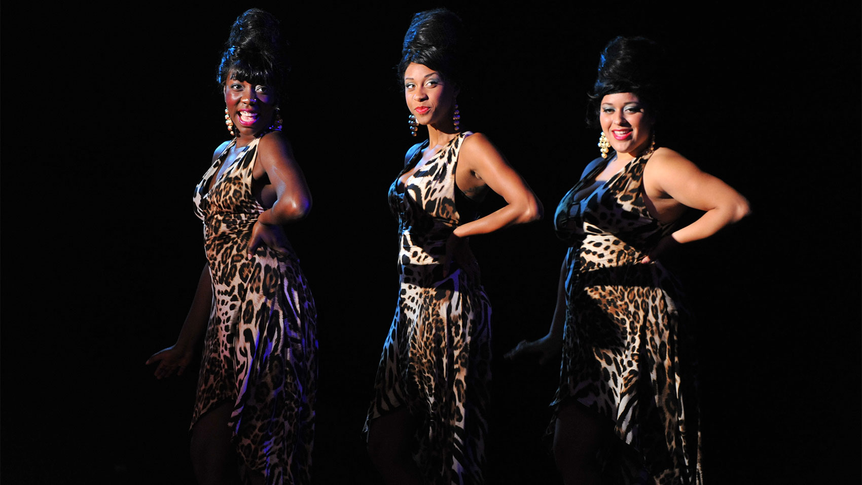 Three women with animal print dresses and beehive hairstyles standing together, each with a hand on their hips