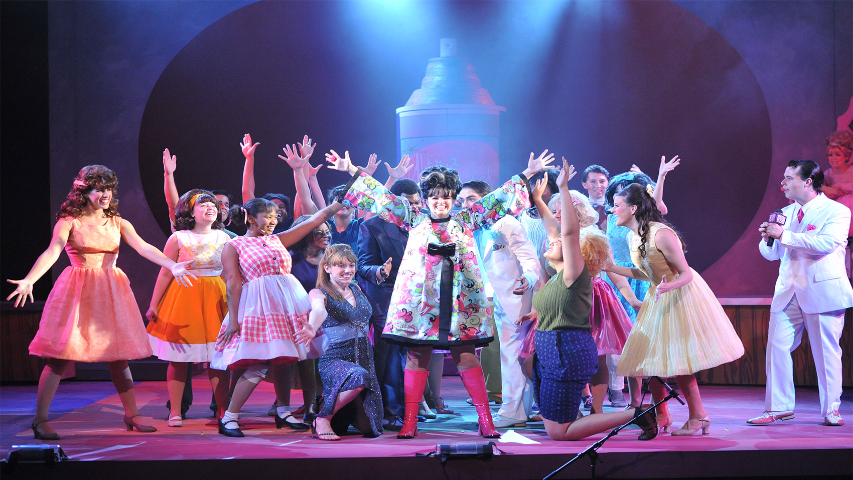 A group of people smiling with their hands up, all looking at one girl in the middle of the stage