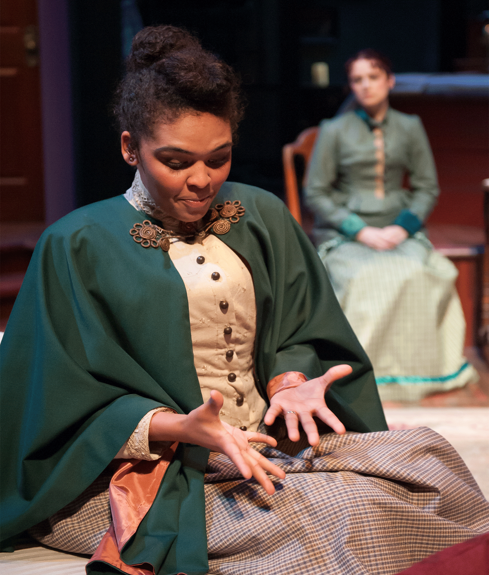 A woman looking down at her hands with another woman sitting behind her