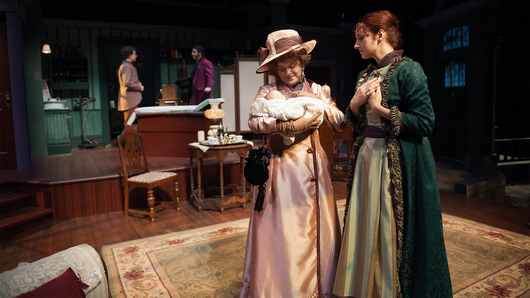 Two women looking at a baby while two men talk in the background