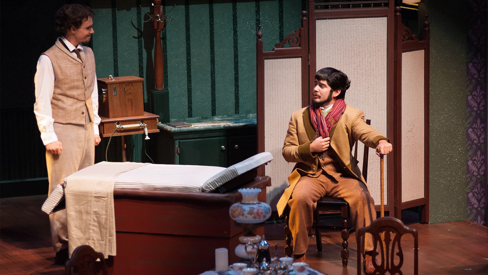 Two men talking to each other, one of them sitting in a chair and resting his hand on a cane