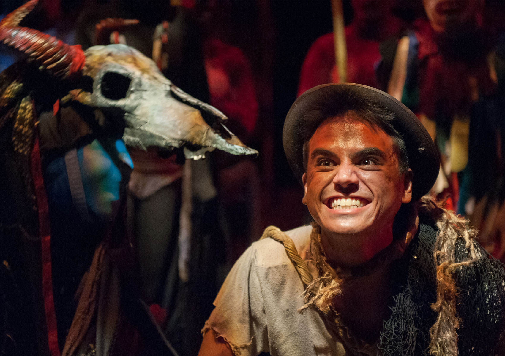 A character grins maniacally while another character holds a longhorn skull that faces the first character, who is looking toward the skull.