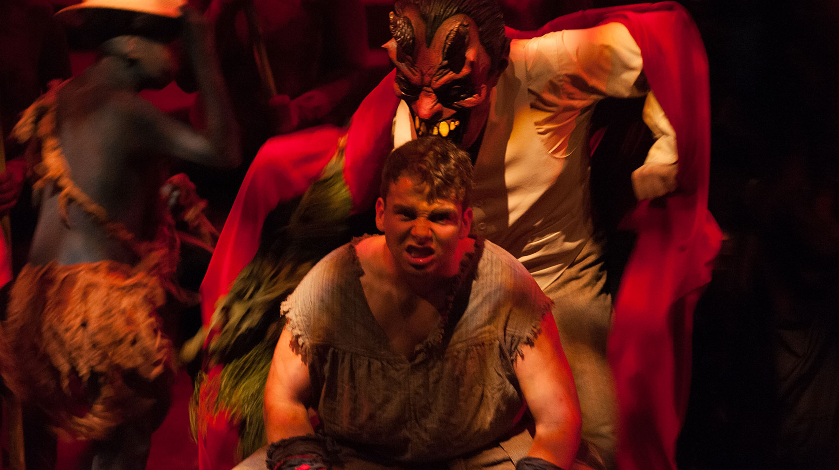 A character snarls facing the audience and is flexing his muscles, while a character resembling a devil figure stands over the first character as if goading him on.