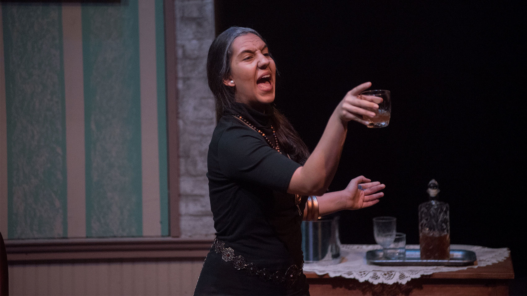 A woman gestures angrily while holding a glass of liquor. 
