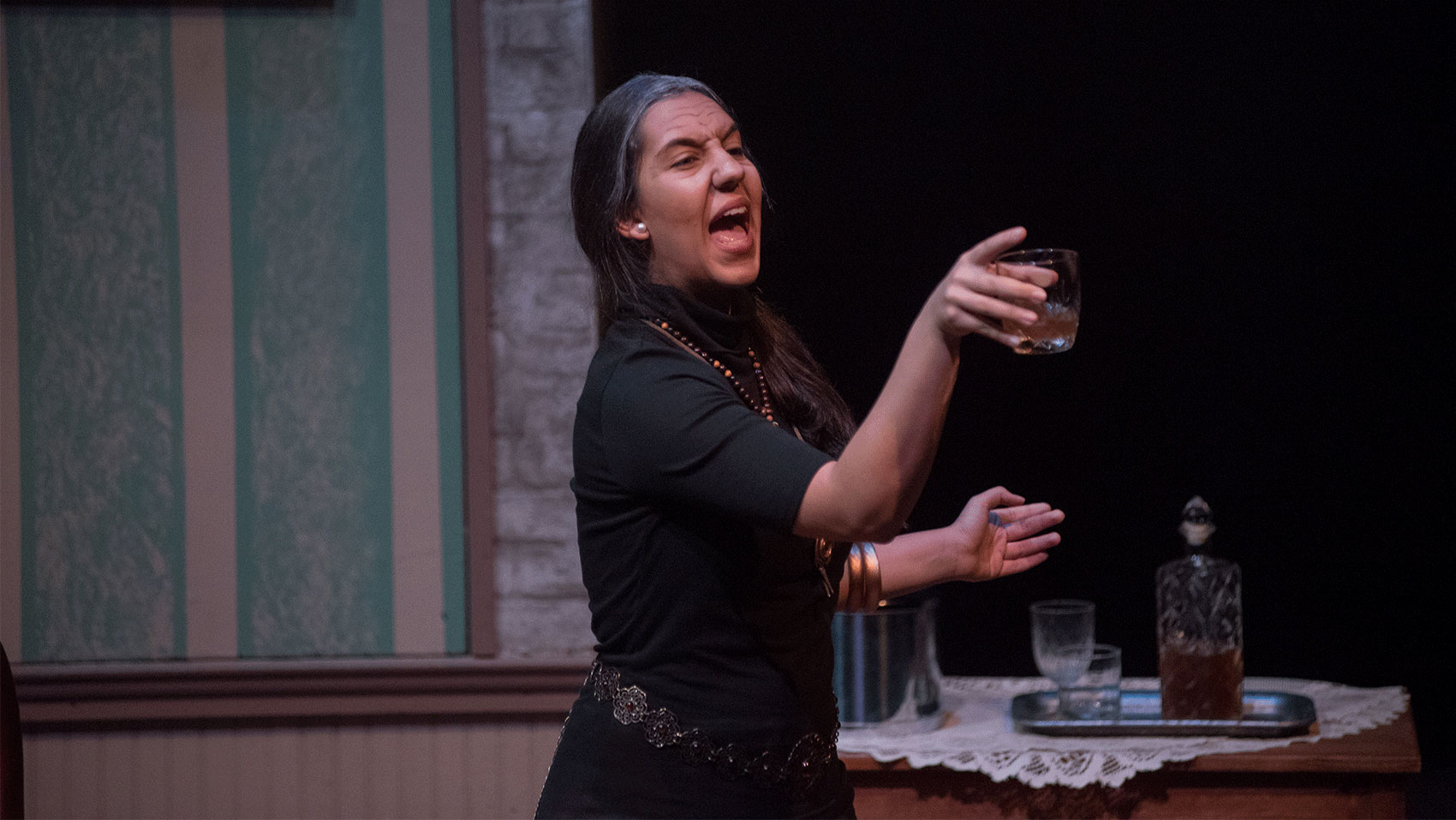 A woman gestures angrily while holding a glass of liquor.