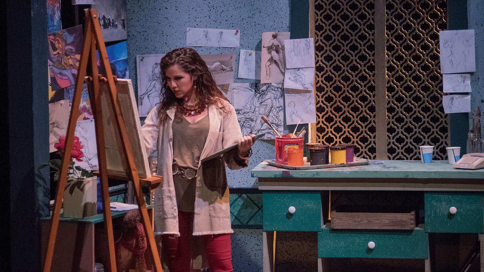 A painter stares intently while working on her canvas and holding what appears to be a palette. 