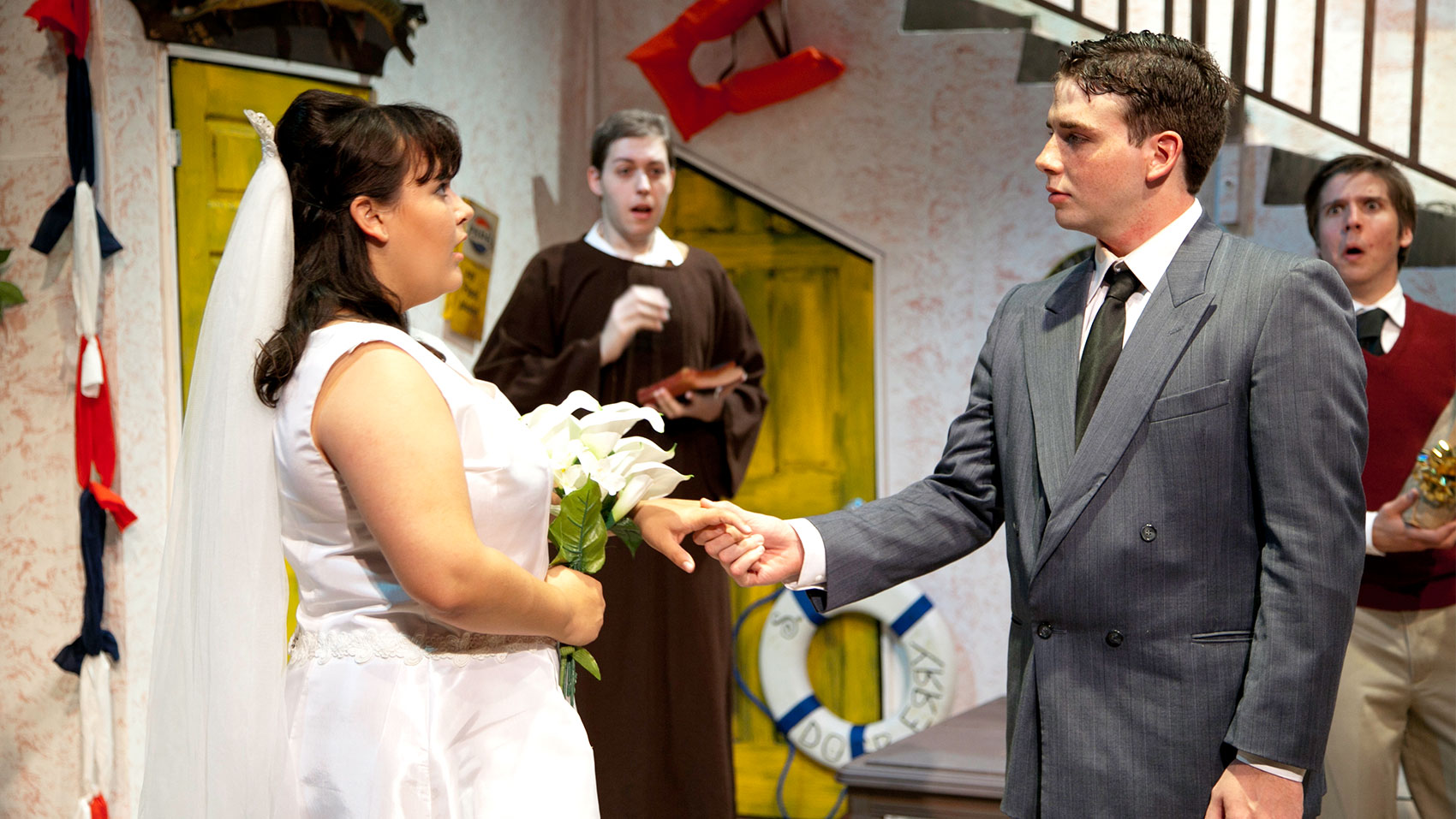 Two characters look on in shock while a man in a suit holds the hand of a woman in a wedding dress holding flowers, who also appears shocked. 