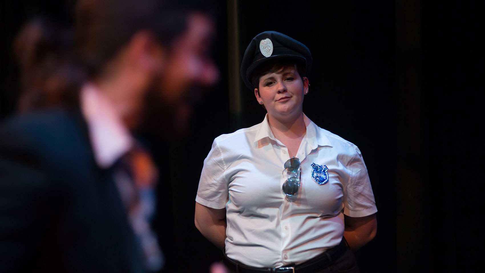 A female cop is watching a male character wistfully in the background, the male character is in the foreground but is out of focus.