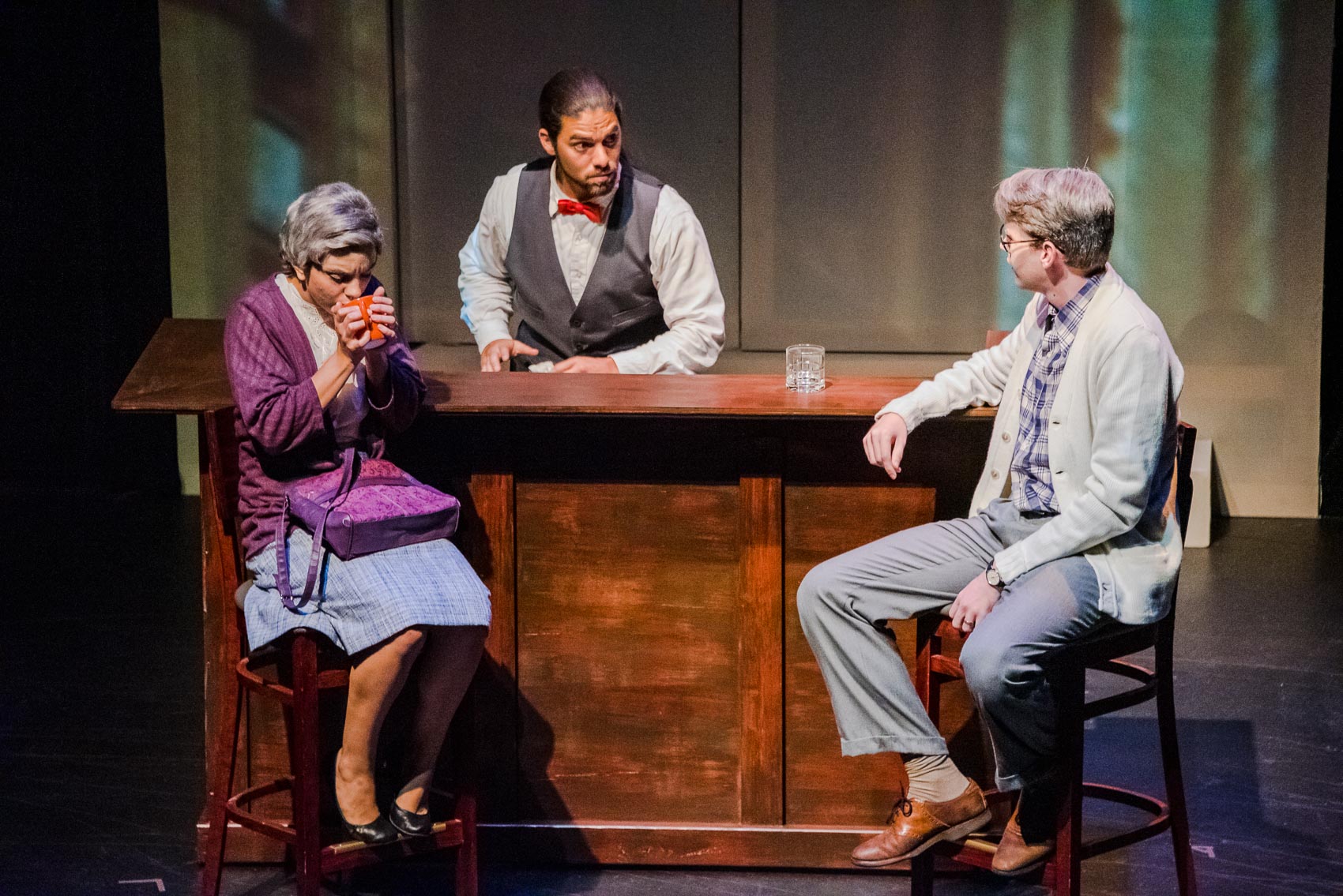 An elderly couple sit at a bar and talk to a bartender.