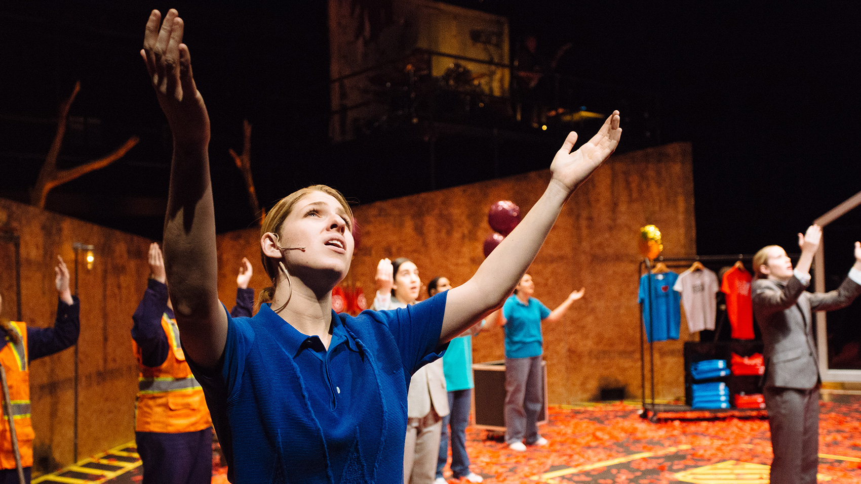 A group of people stand with their arms and hands raised to the ceiling, as if speaking to someone or something above them.