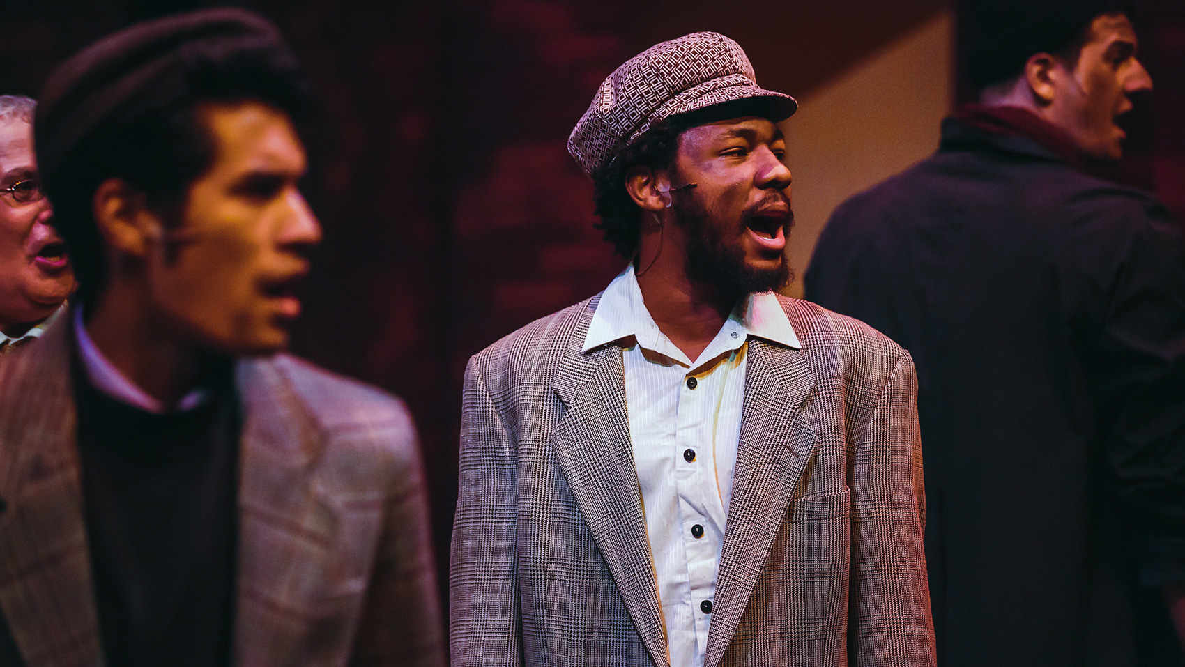 A close up of four men standing, looking to the right (audience's right), speaking. 