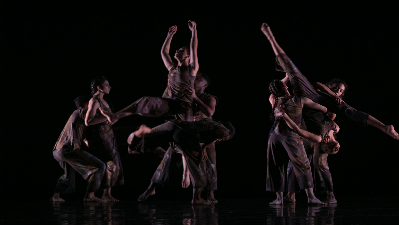 Two dancers are lifted separately in the air, supported by other dancers. One of them is doing an upside-down split. 