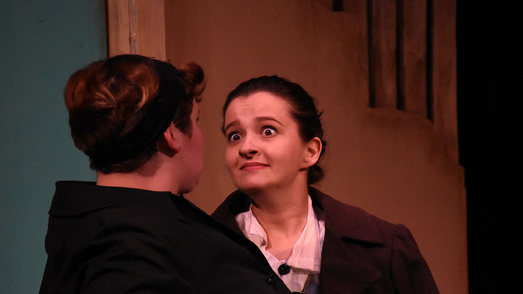 Two women face each other, one leaning forward into the other's face, her eyebrows raised with a questioning, almost intimidating look on her face.