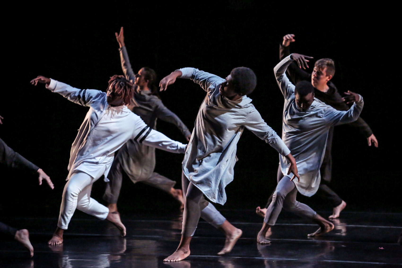 Dancers take a step, side by side, in a line with their arms out, leaning back.