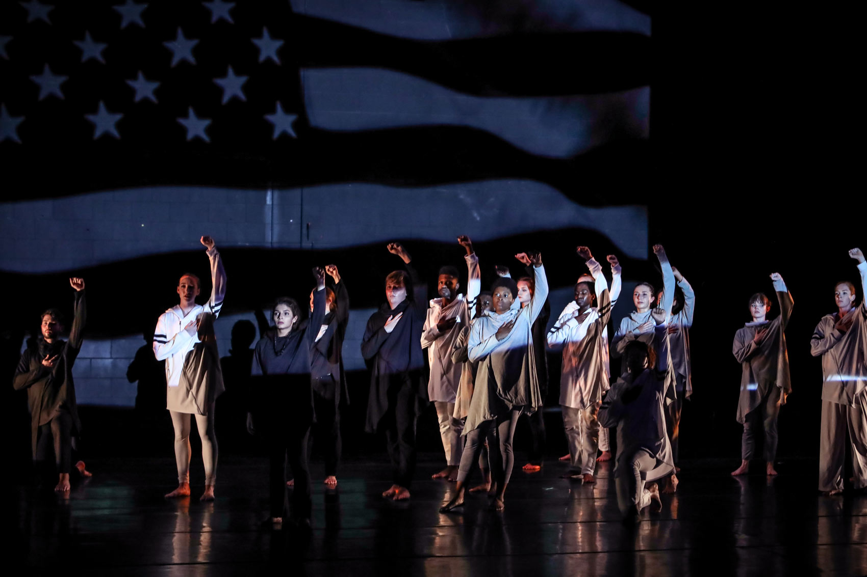 Dancers stand with their fists in the air while the US flag is projected over them.