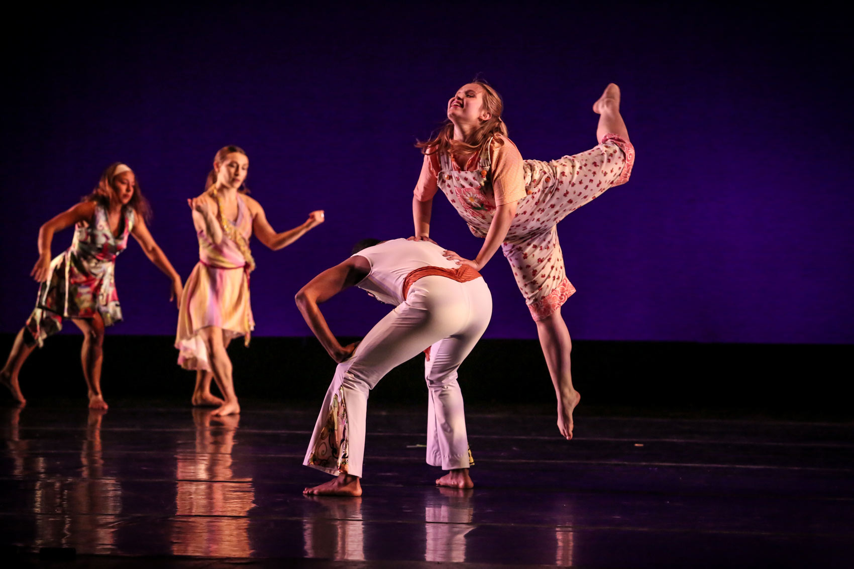 A dancer leaps up joyfully while using the back of another dancer for support.