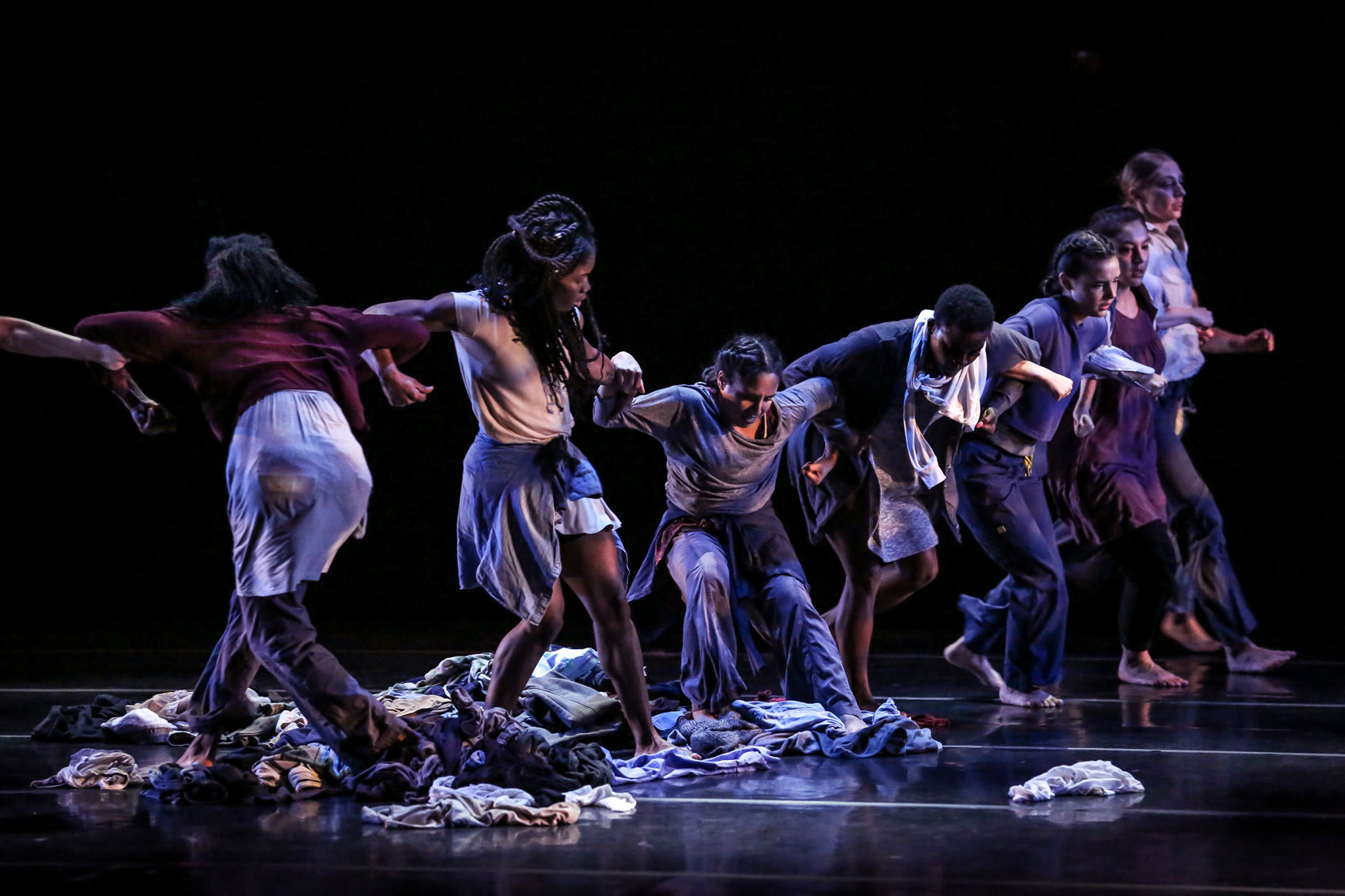 Dancers stand together with interlocked arms.