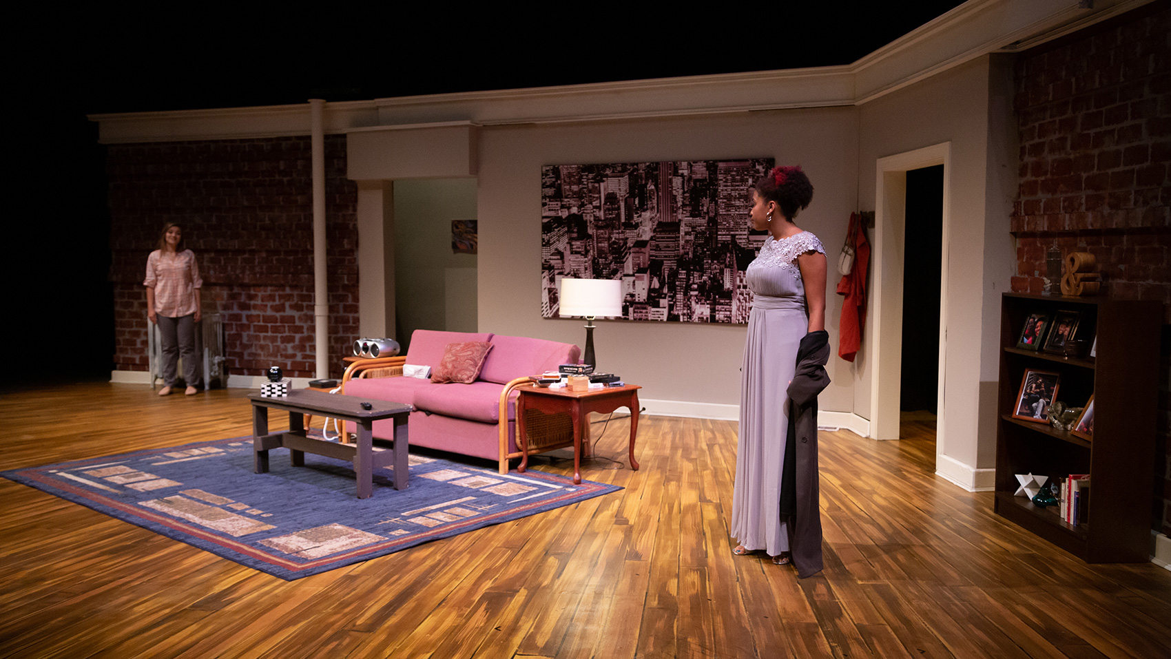 Two women look at each other from across the living room of an apartment.