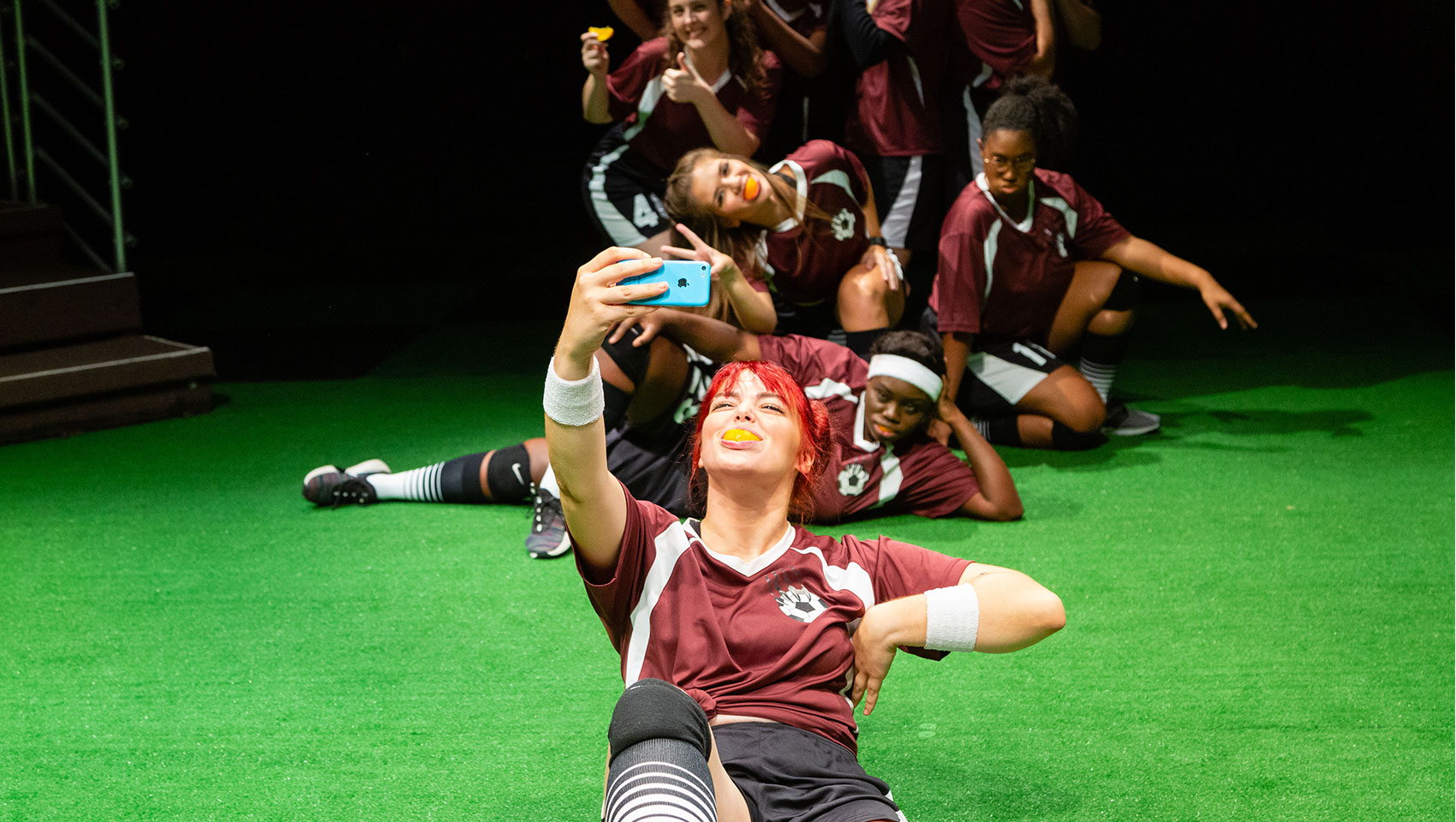 A girls' soccer team take a silly group pic together, some of them smiling with orange peels covering their teeth.