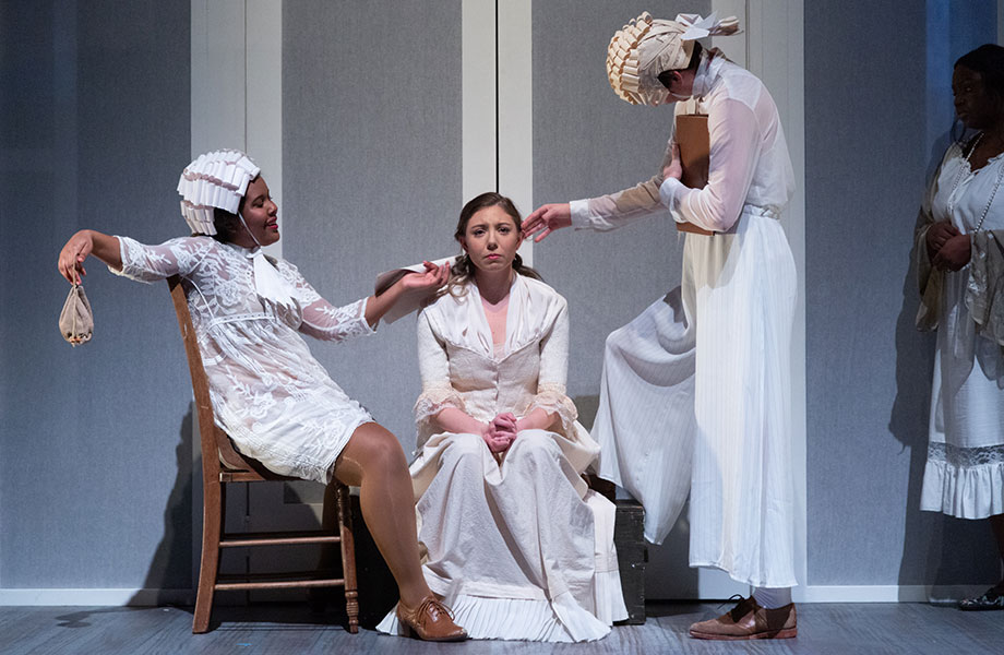 Image from TheatreUSF's adaptation of Virginia Woolf's "Orlando." The main character sits with a forlorn expression on their face, one person to each of their side either comforting or taunting them.