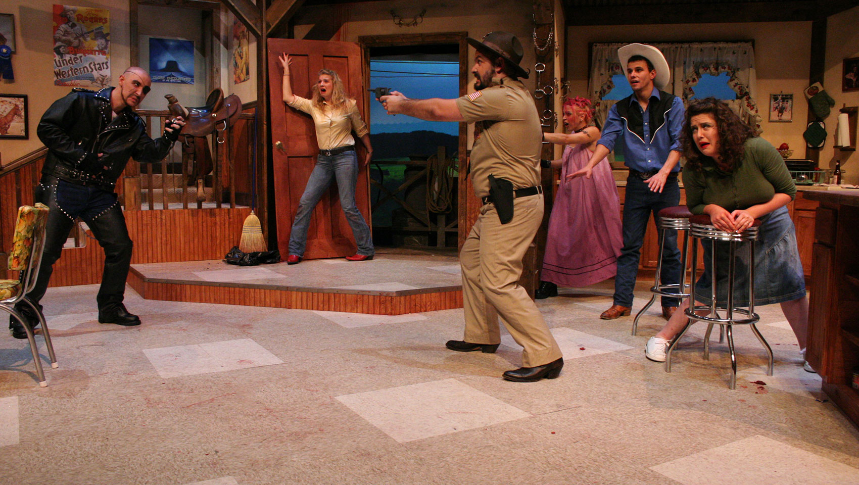 A sheriff points his gun at a man wearing a leather jacket, as other people look on in fear and shock.
