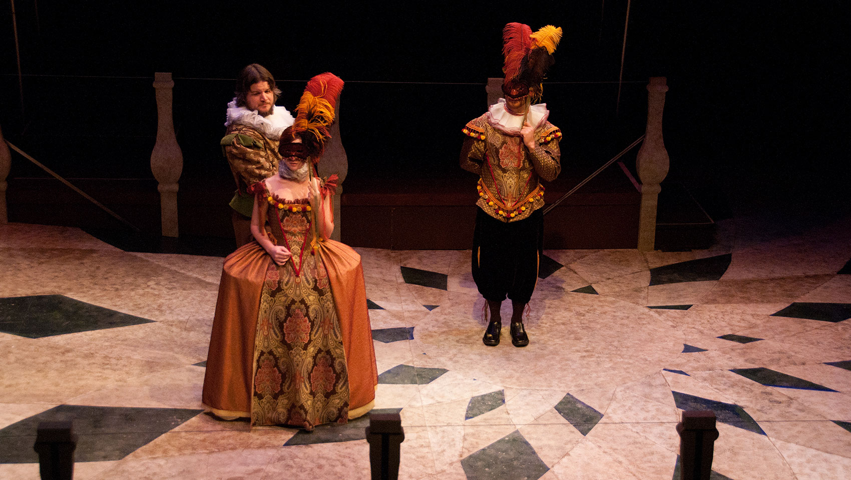 Three people dressed in upper-class 17th century attire speak together. 