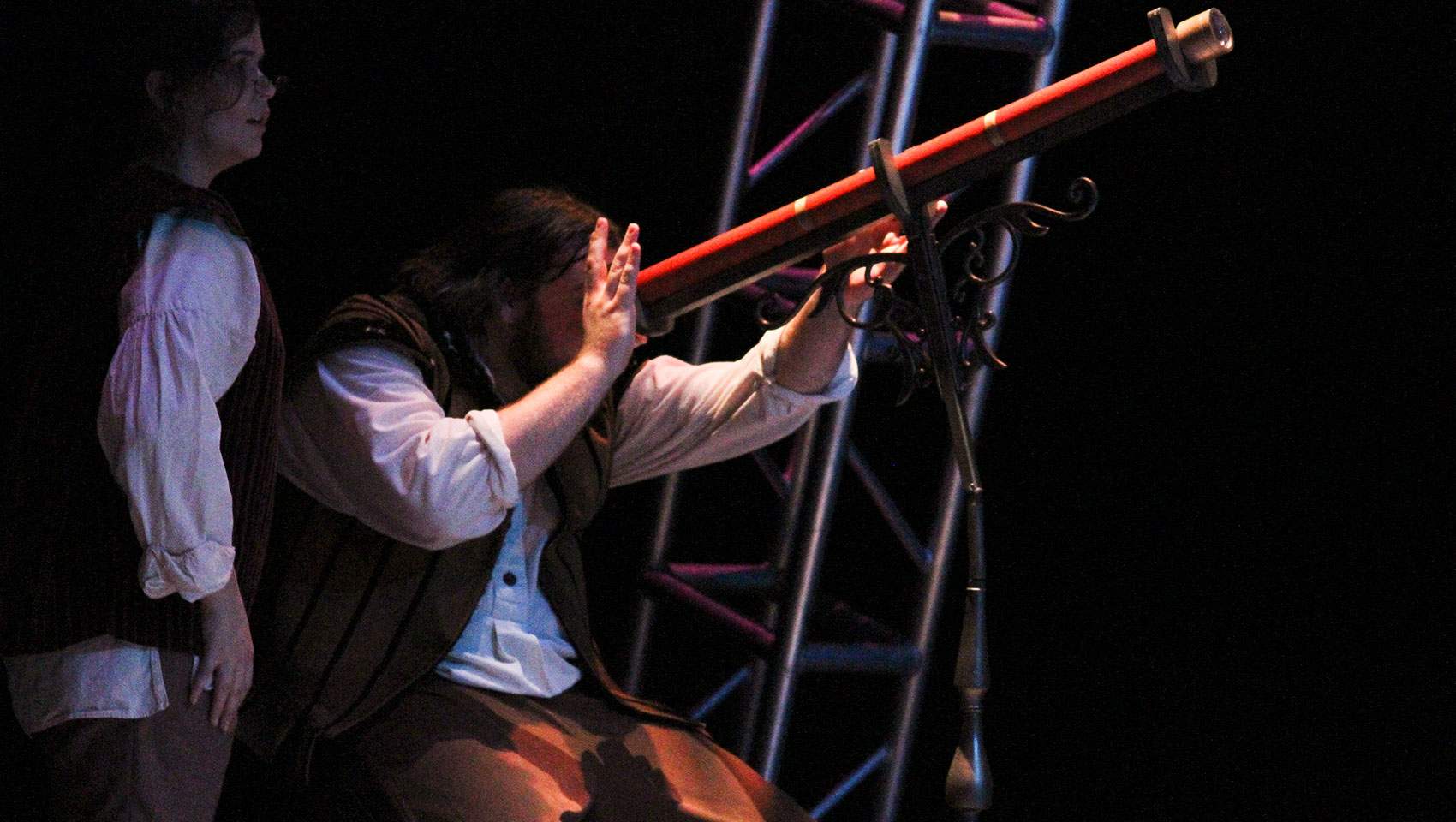 A man peers through a large red telescope.