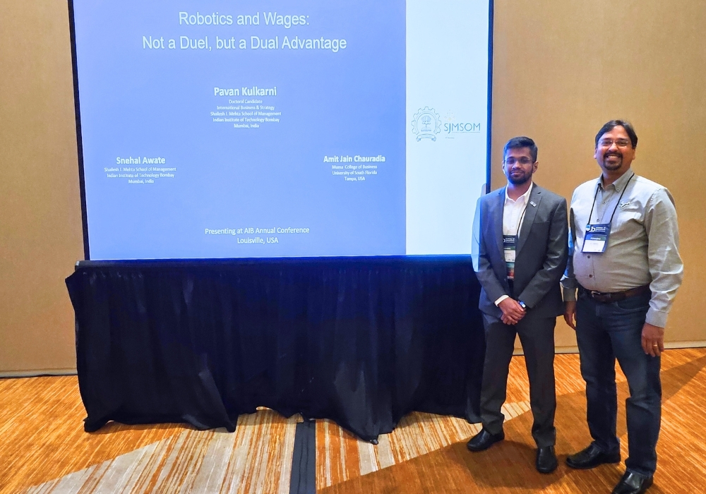 Chauradia and Kulkarni stand in front of a sign promoting their research presentation.