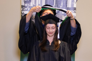 graduate bending down to get hooded for their master's degree ceremony.
