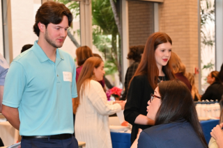 Male student speaking with woman seated at a vendor table.