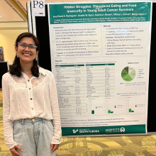 woman smiling at camera, standing in front of research poster