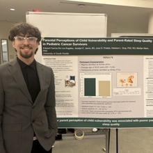 Young man smiling, standing in front of research poster.
