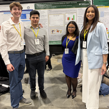 group of four students standing with presenting poster.