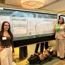 Two women on either side of a research poster, smiling at camera