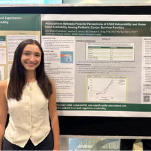 Young woman in front of research poster, smiling.