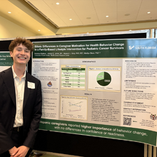 young man smiling, standing in front of research poster