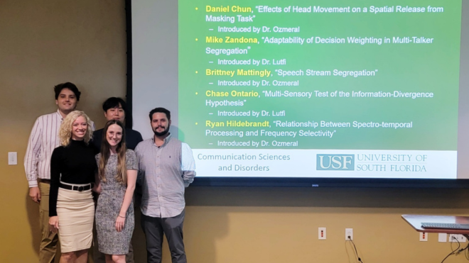 Audiology students stand in front of a projected slide that shows the morning's list of presenters.