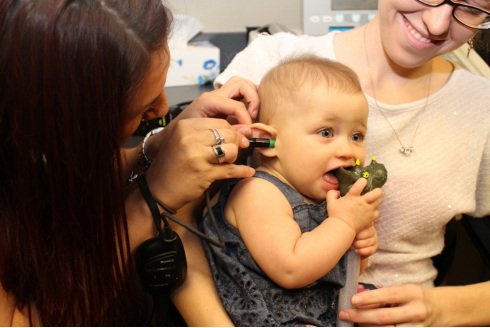Infant holding a dinosaur toy is checked for hearing loss