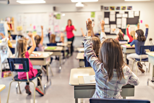 Young students in a classroom with hands raised