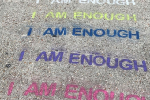 The phrase, “I am enough,” stamped in multiple colors on the pavement.