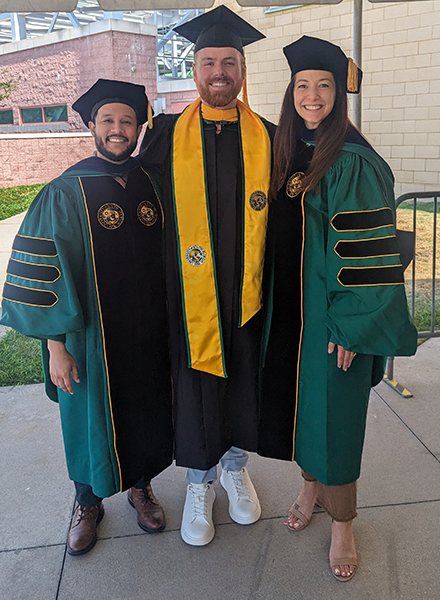 Jeffrey Centeno-Jerviss and two faculty members in caps and gowns