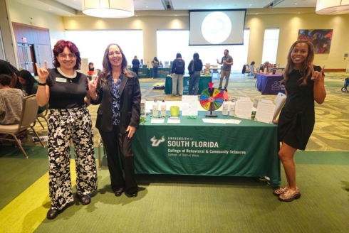 Valentina Arcilia, VickiLynn, and Sandra Accilien in front of the School of Social Work table