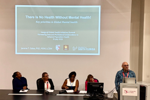 Jerome Galea speaks at a podium with four other speakers behind him