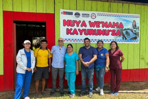 Jerome Galea standing with his colleagues in front of a brightly painted green and red wooden building.