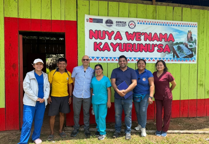 Jerome Galea standing with his colleagues in front of a brightly painted green and red wooden building.